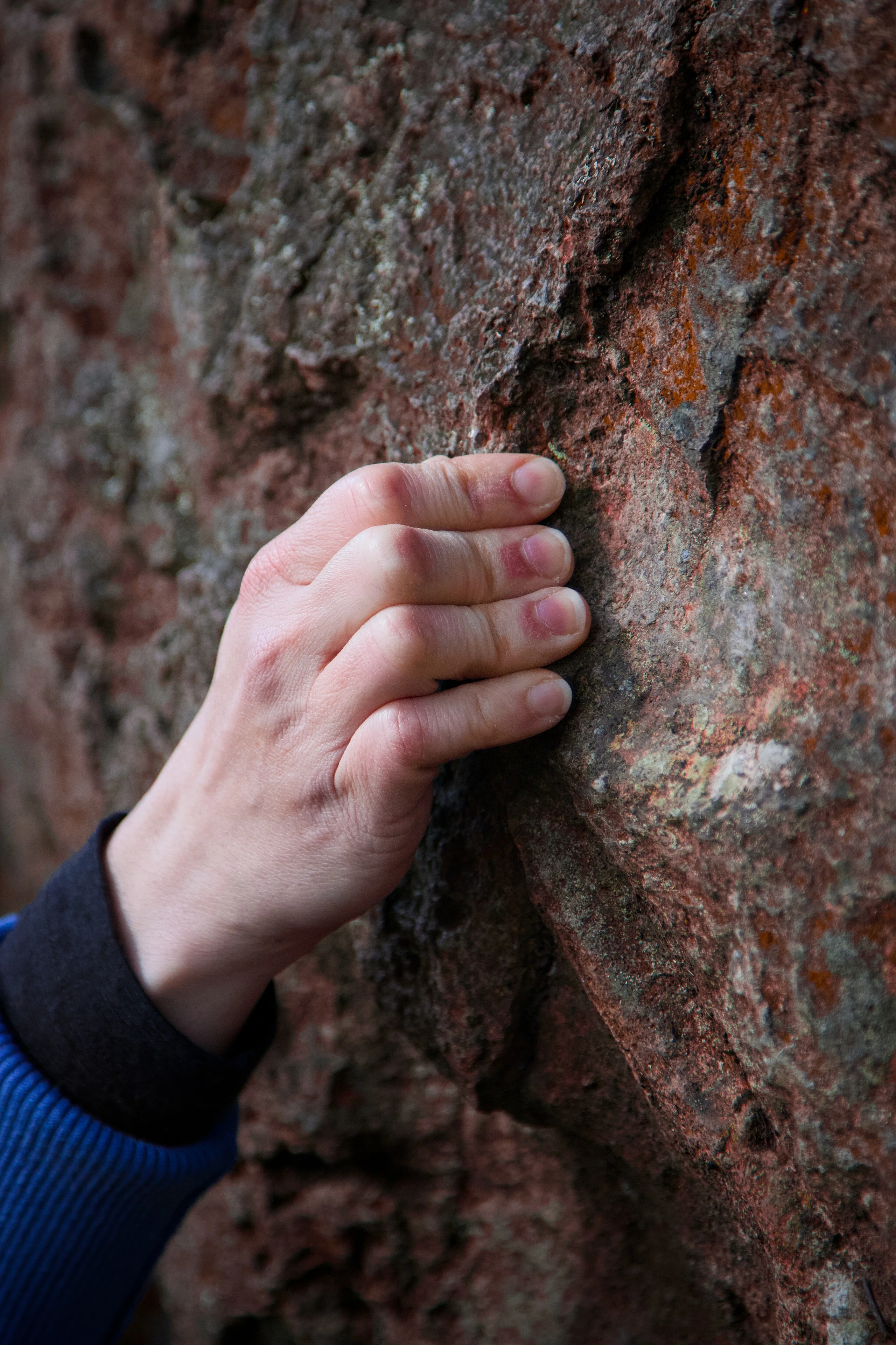 A close view of a climber's hand gripping a small hold on textured rock.
