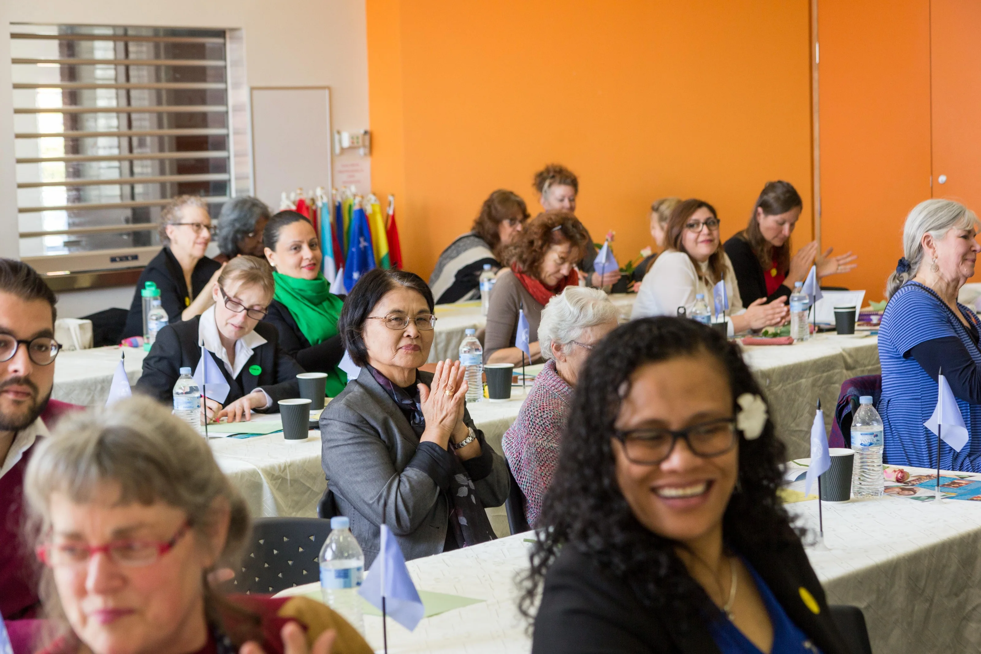Guests smile and applaud while seated around tables in a bright community room.