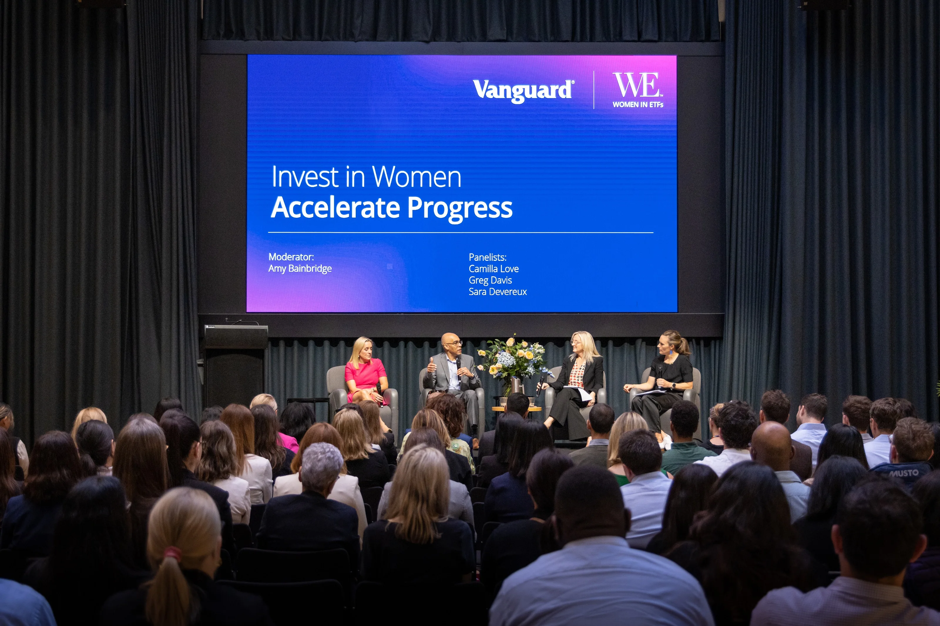 An audience watches four panellists beneath an Invest in Women Accelerate Progress screen.