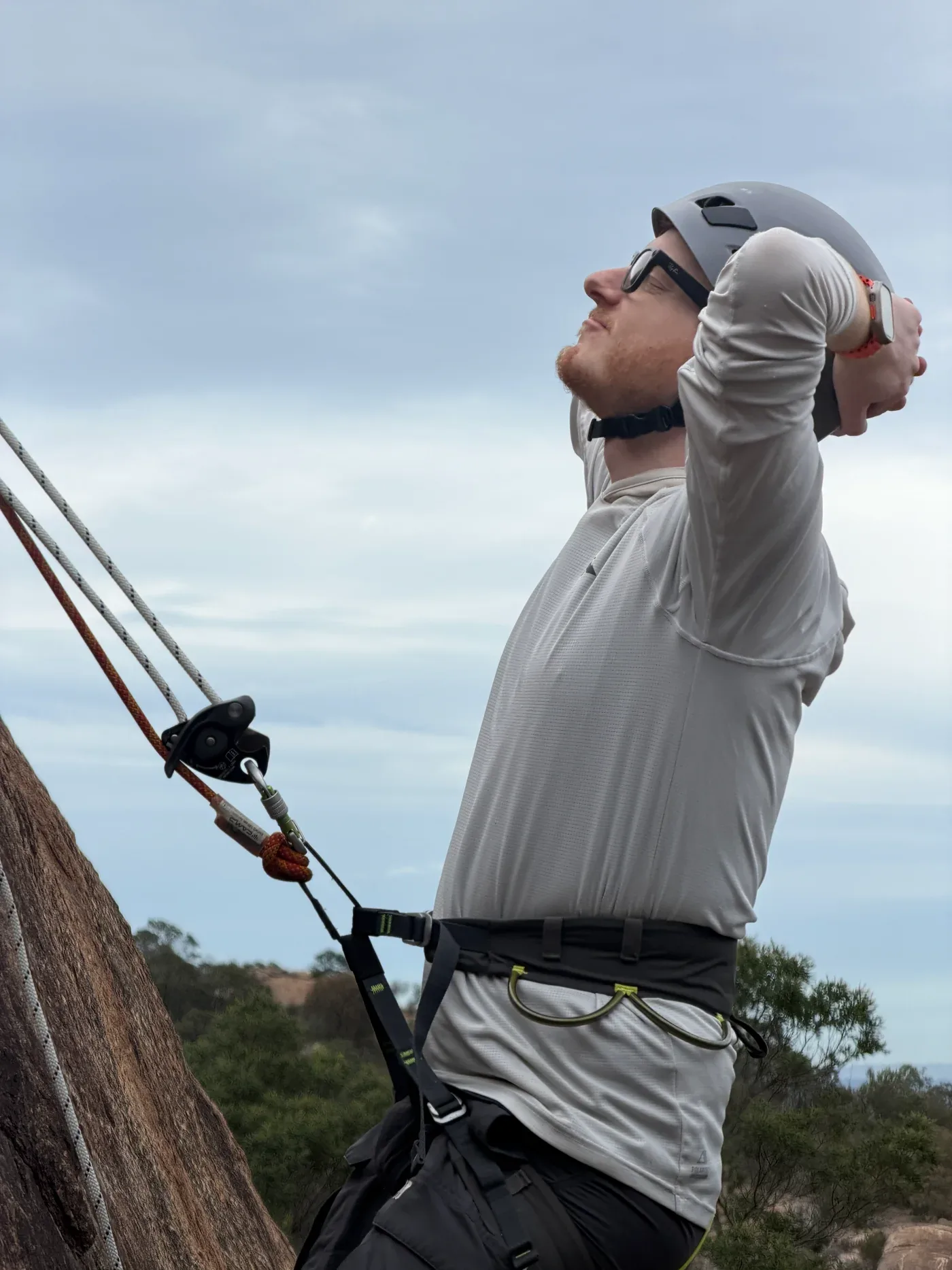 A climber in a helmet and sunglasses taking a break beside the rock face.