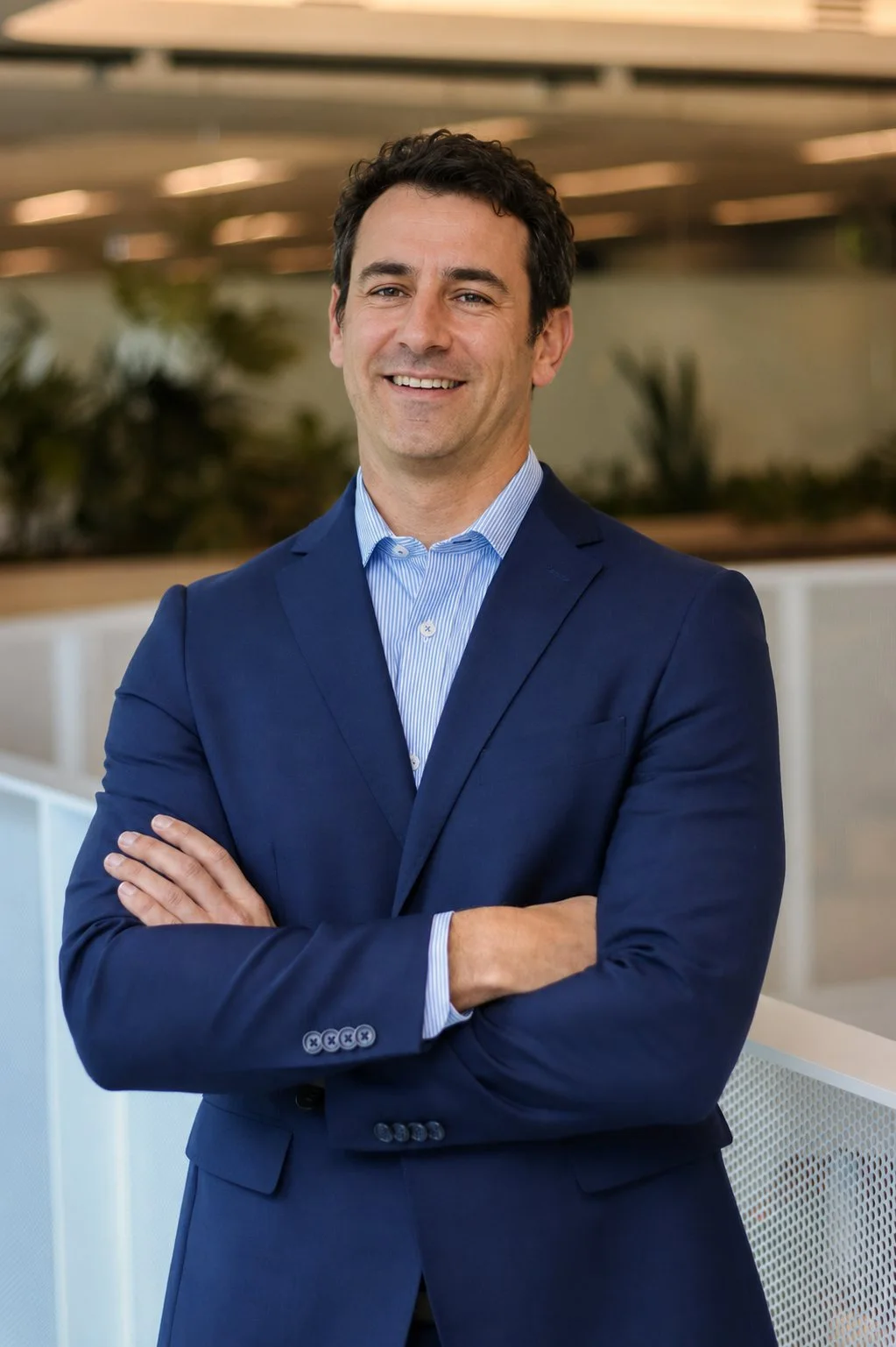 Professional portrait of a man in a blue suit with folded arms.