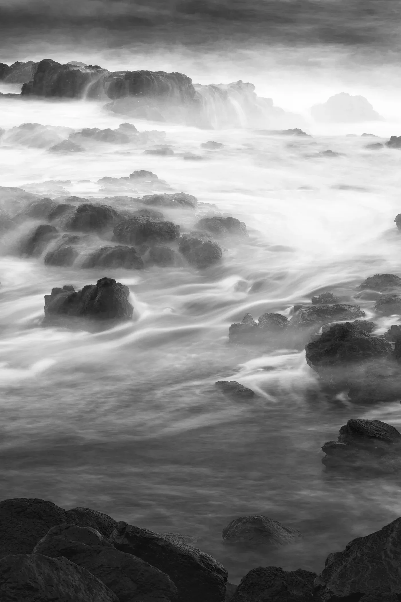 Black-and-white photograph of water flowing around coastal rocks.
