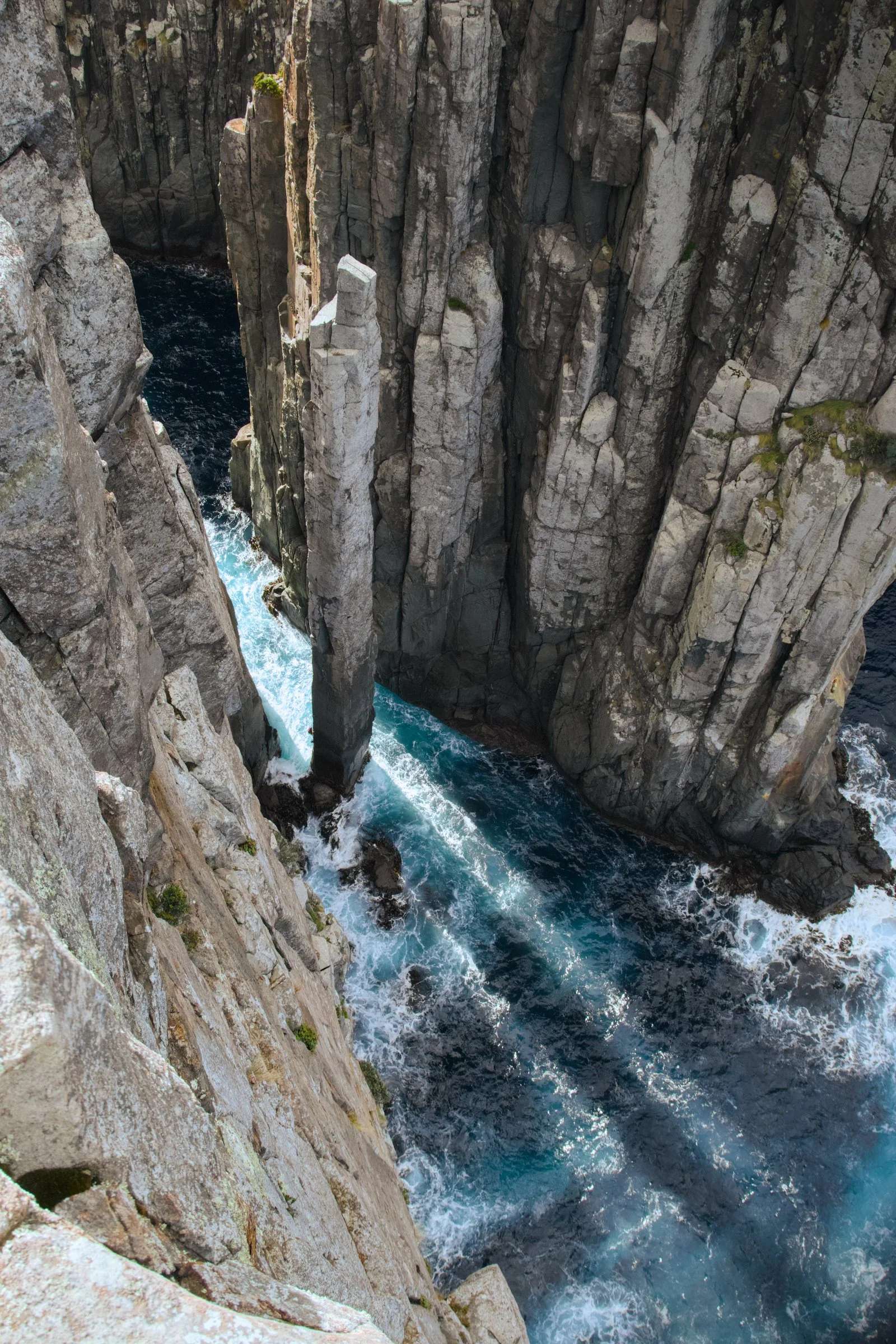 Blue water runs through a narrow coastal rock chasm.