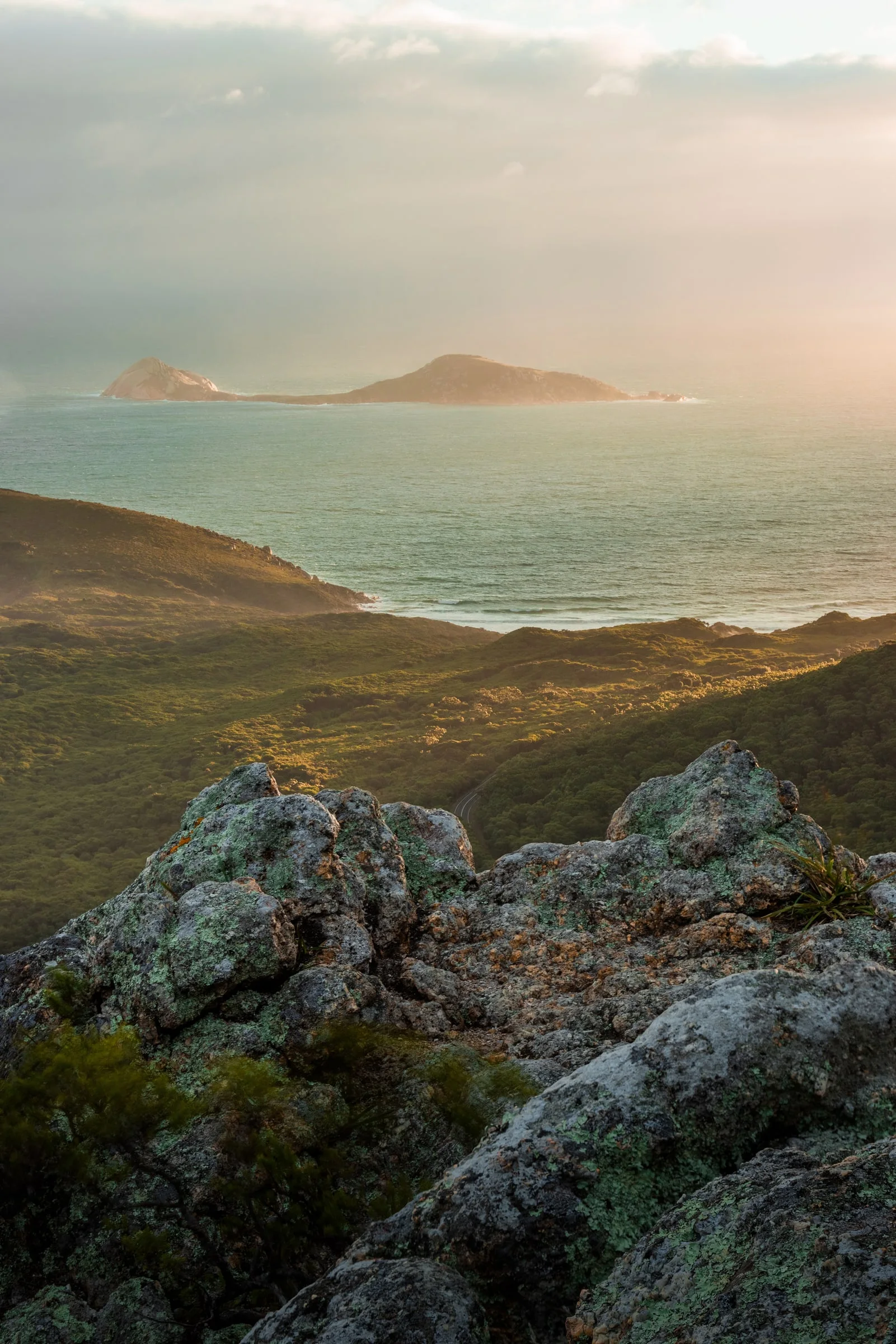 Offshore islands sit beneath rain and sunlight, framed by lichen-covered rocks.