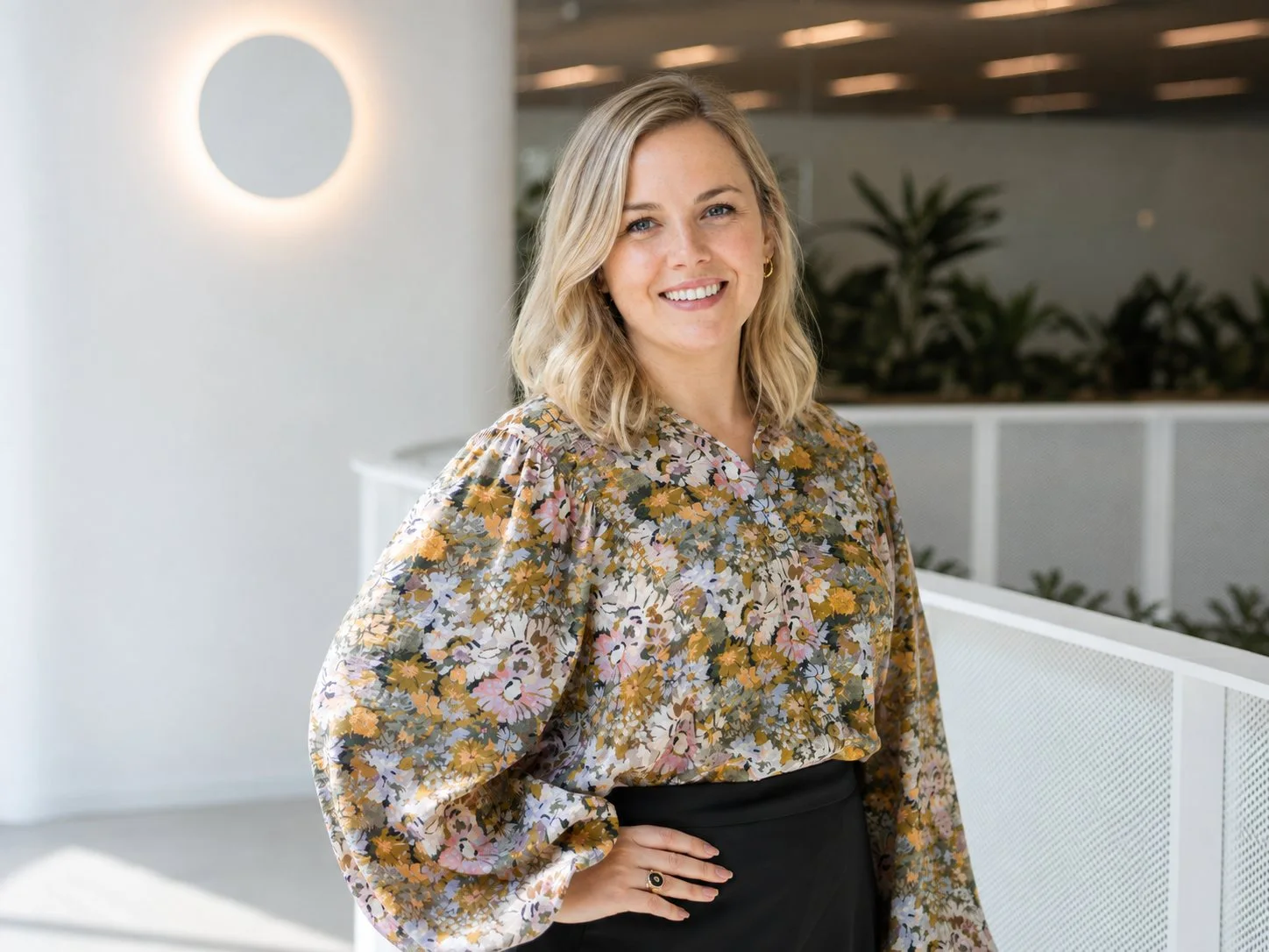 Professional portrait of a woman in a patterned blouse in a modern office.