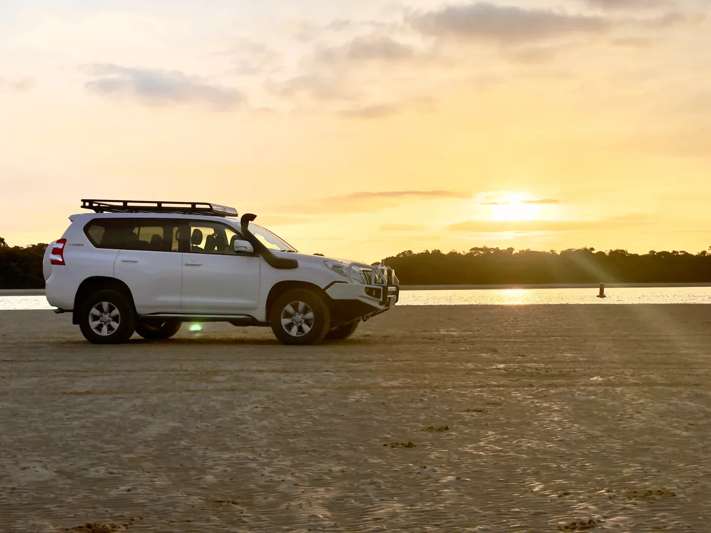 A four-wheel drive parked beside the water in the golden evening light.